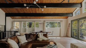 Un amplio salón con un sofá de cuero marrón, techo de madera y ventanas grandes.