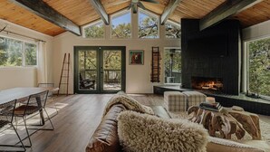 Un interior acogedor con chimenea, techo de madera y vistas a una terraza exterior a través de puertas de cristal.