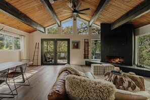 Ein gemütliches Interieur mit Kamin, Holzbalkendecke und Blick durch Glastüren auf eine Außenterrasse.