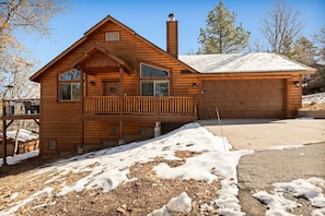 A wooden cabin with a balcony, a garage, and a chimney. - Oak Tree Lodge, w/ Hot Tub, Fire Pit, Game Room (Big Bear)