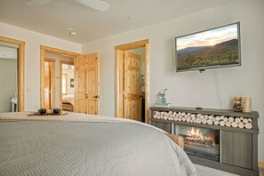 A bedroom with a bed, a fireplace, a television mounted on the wall, and wooden doors. - Oak Tree Lodge, w/ Hot Tub, Fire Pit, Game Room (Big Bear)