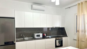 Een moderne keuken met witte kastjes, een zwarte marmeren spatwand, een magnetron, een waterkoker en een kleine oven.