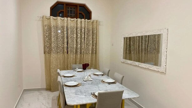 Un'area pranzo con un tavolo in marmo apparecchiato per quattro persone, una tenda decorata e uno specchio ornamentale al muro.