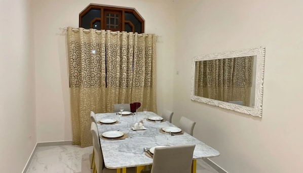 A dining area with a marble table set for four, a patterned curtain, and a decorative mirror on the wall.
