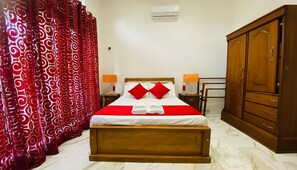 A neatly made bed with red and white bedding, a wooden wardrobe, and a red patterned curtain. - Silva Villa Negombo #3 (Negombo)