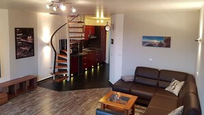 A modern living room with a brown sofa, a wooden coffee table, and a staircase leading to a kitchen area. - Apartment 'Meerblick' with Sea View, Balcony and Wi-Fi (Horumersiel-Schillig)