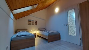A bedroom with two beds, a wooden ceiling, a wall-mounted light, and a door with a patterned glass panel. - Apartment 'Meerblick' with Sea View, Balcony and Wi-Fi (Horumersiel-Schillig)