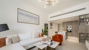 Un salon moderne avec un canapé blanc, une table basse et un coin repas, la cuisine étant visible au fond.