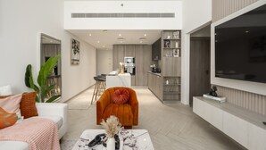 Un salon moderne avec un canapé blanc, un fauteuil orange, une table basse et un téléviseur fixé au mur.