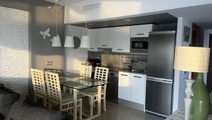 Una cocina moderna con comedor, con una mesa de vidrio, armarios blancos y electrodomésticos de acero inoxidable.