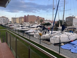 A marina with multiple boats docked, a grassy area, and buildings in the background. - Apartment in luxury residence with direct view of Santa Margarita canals (Roses)