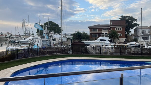 Un puerto deportivo con barcos amarrados, una piscina y edificios residenciales al fondo.