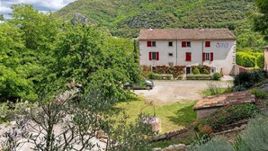 A two-story building with a red-tiled roof, surrounded by lush greenery and a mountainous backdrop. - Guest Room “La Drosera - Room No.6” with Shared Terrace, Garden & Wi-Fi (Riols)