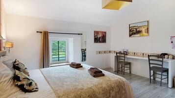 Une chambre d’hôtel comprenant un lit, un bureau, deux chaises, une fenêtre avec des rideaux et des œuvres d’art accrochées aux murs.