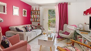 Een woonkamer met een bank, stoelen, een salontafel, een boekenkast en uitzicht door een glazen deur.