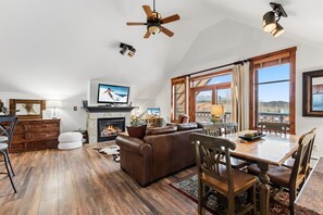 A spacious living room with a fireplace, a large window with a view, and a ceiling fan. - Cozy Retreat Steps Away From Vibrant Downtown Breckenridge! (Breckenridge)