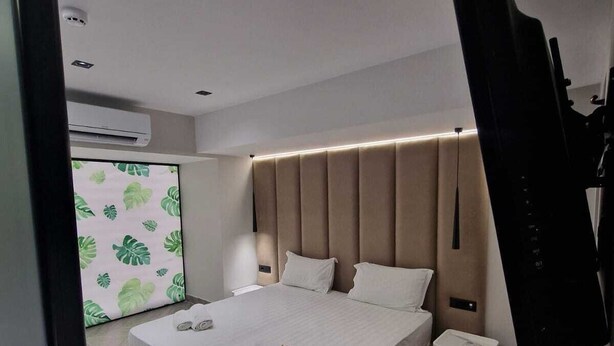 A modern bedroom with a large bed, a flat-screen TV mounted on the wall, and a small bedside table.