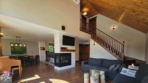 Un vaste espace de vie doté d’une cheminée, d’un escalier et d’un coin repas offrant une vue sur l’extérieur.