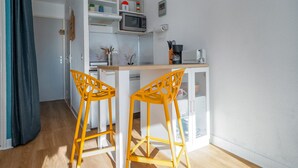 Cocina pequeña con armarios blancos, un microondas, una cafetera y dos taburetes amarillos.
