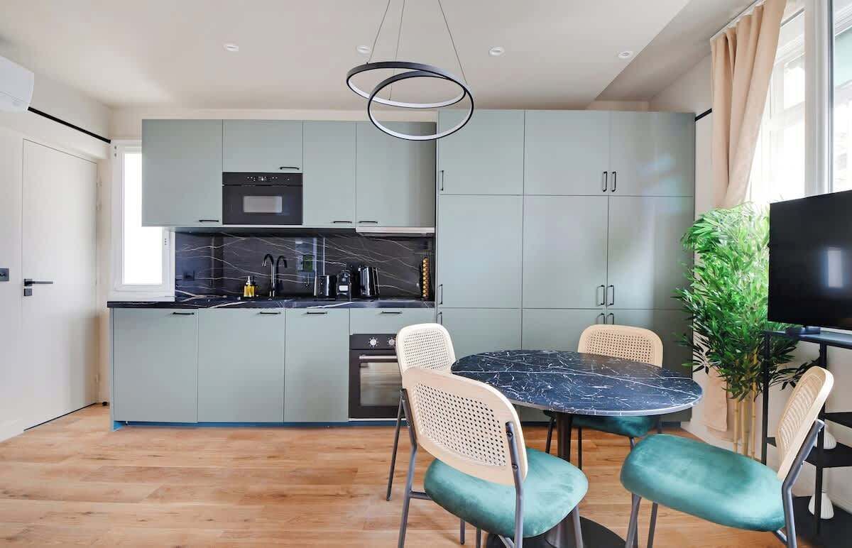 A modern kitchen with grey cabinets, a black countertop, and a round dining table with four chairs.