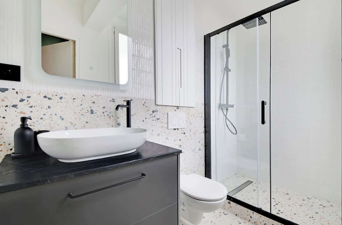 A modern bathroom with a white vessel sink, black countertop, and a glass-enclosed shower.