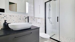 Une salle de bain moderne avec un lavabo sur colonne blanc, un plan de toilette noir et une douche à parois de verre.