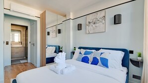 Habitación de hotel moderna con una cama grande, un espejo, obras de arte en la pared y una pequeña planta en la mesita de noche.