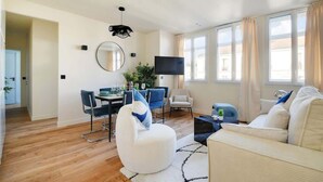Una sala de estar moderna con comedor, un televisor de pantalla plana y ventanas amplias con cortinas.