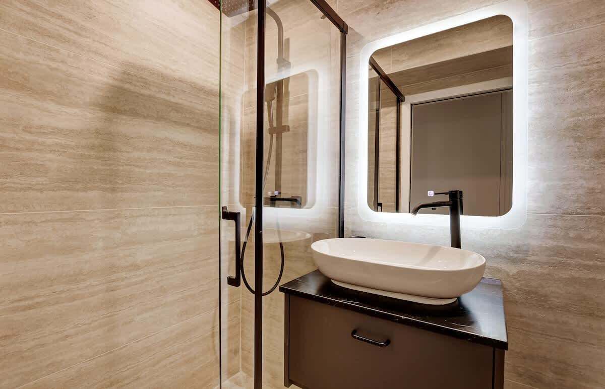 A modern bathroom with a glass shower enclosure, a large mirror, and a vessel sink.