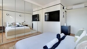Una habitación de hotel moderna con una cama grande, un televisor montado en la pared, un armario con espejo y una mesita de noche pequeña.
