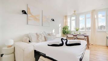 A modern hotel room with a large bed, a sofa, a dining area, and artwork on the walls.
