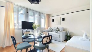 Una sala moderna con comedor, sofá, televisor de pantalla plana y un amplio ventanal con cortinas.