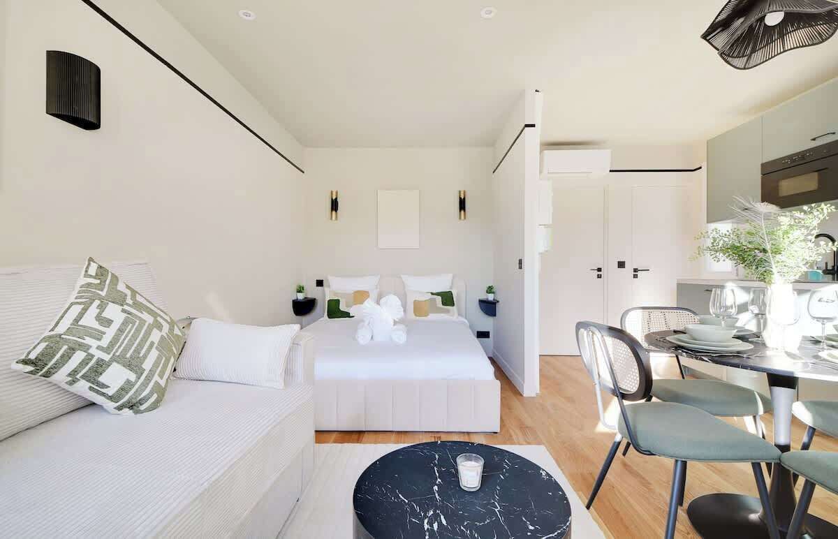 A modern bedroom with a large bed, a sitting area with a couch, and a dining area with a table and chairs.
