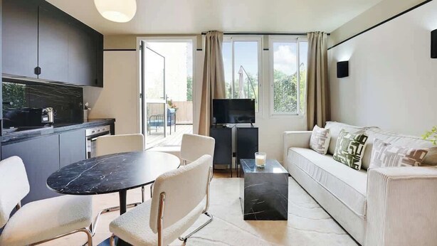 Ein modernes Wohnzimmer mit einer Couch, einem Esstisch mit Stühlen, einem Fernseher und einer Küchenzeile mit Schränken und einer Arbeitsplatte.