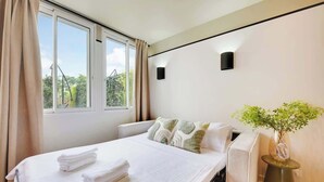 Ein modernes Hotelzimmer mit einem großen Bett, einem Nachttisch mit einer Vase und Blick auf Grünfläche.