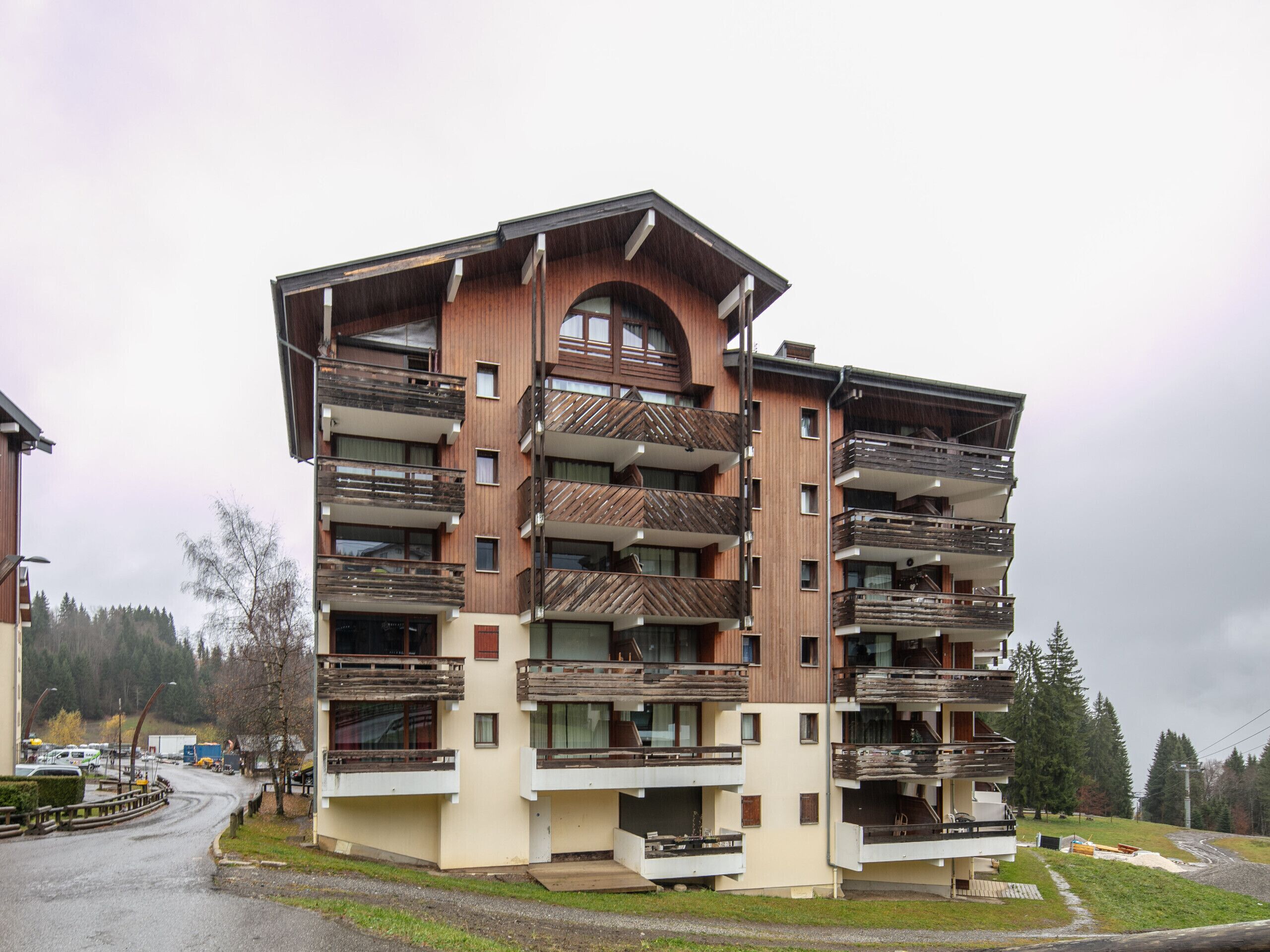 A multi-story building with balconies, a central atrium, and a parking area in the foreground.