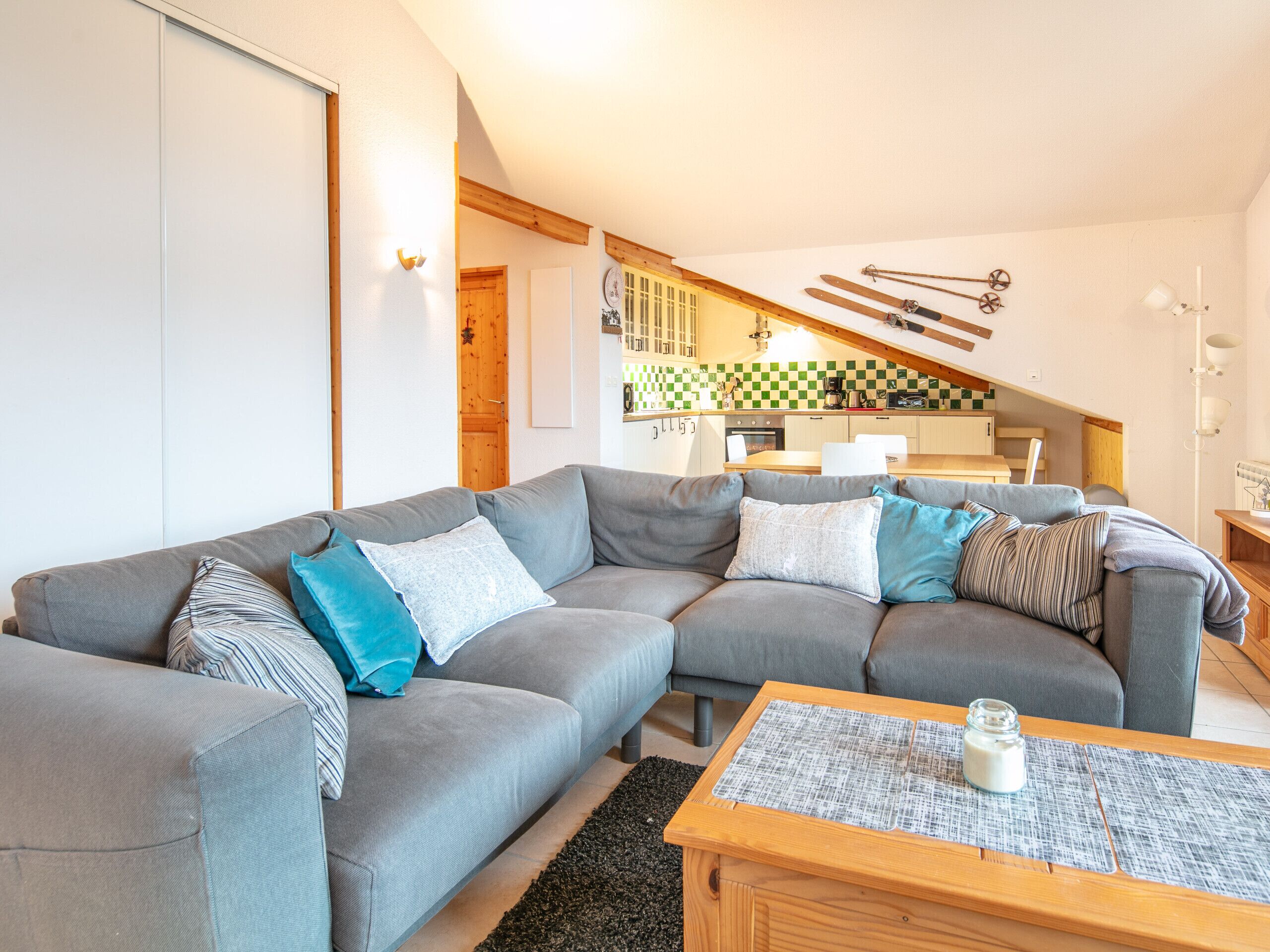 A modern living room with a grey sectional sofa, a wooden coffee table, and a kitchen in the background.