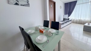 Ein Essbereich mit Tisch für vier Personen, einem Fernseher im Hintergrund und einer Tür rechts.