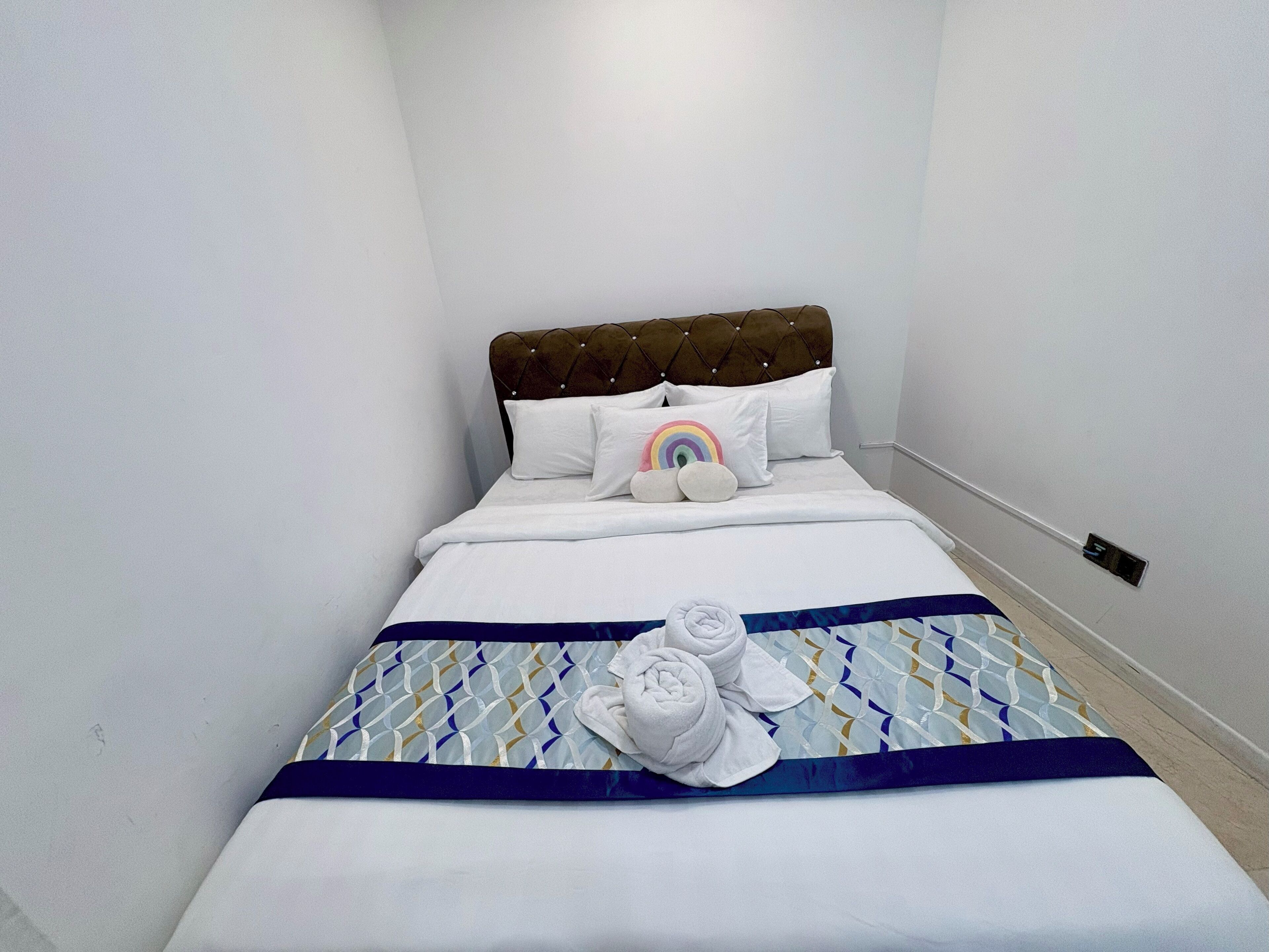 A neatly made bed with a patterned bedspread, pillows, and a rolled towel on the bed.