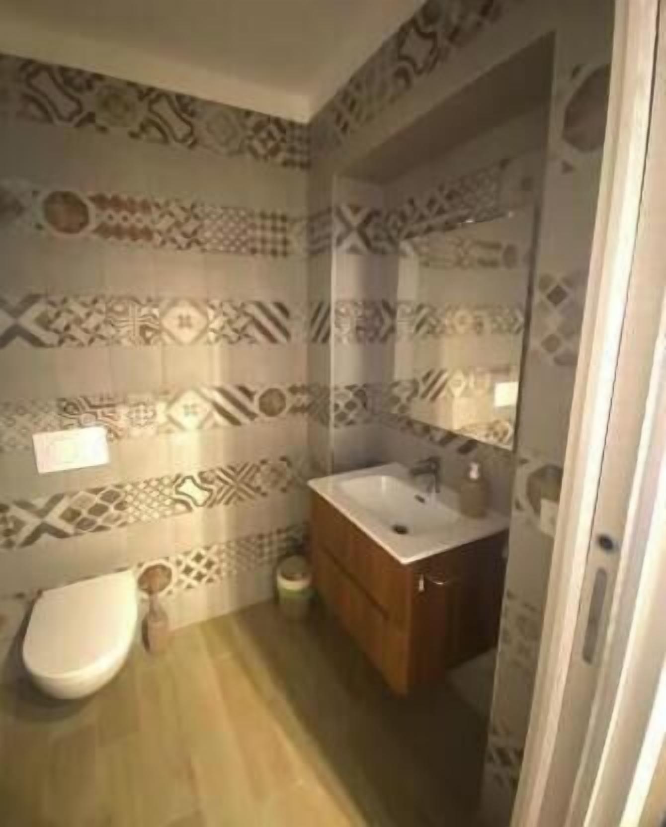 Een badkamer met betegelde vloer, een wit toilet, een houten kastje en een wastafel.