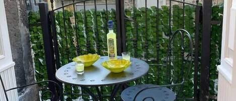 Une petite terrasse extérieure avec une table ronde et deux chaises, entourée d’une clôture en fer forgé noir.