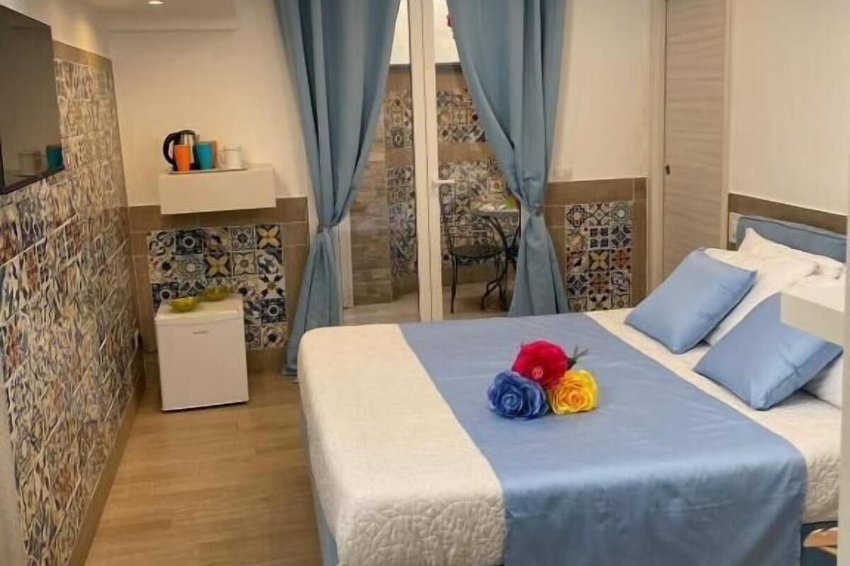 A bedroom with a bed, curtains, a nightstand, a small table, and a ceiling light.