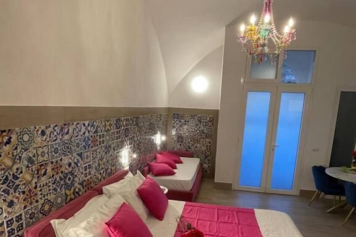 A bedroom with a large bed, two smaller beds, a chandelier, and a view of the sky through the window.