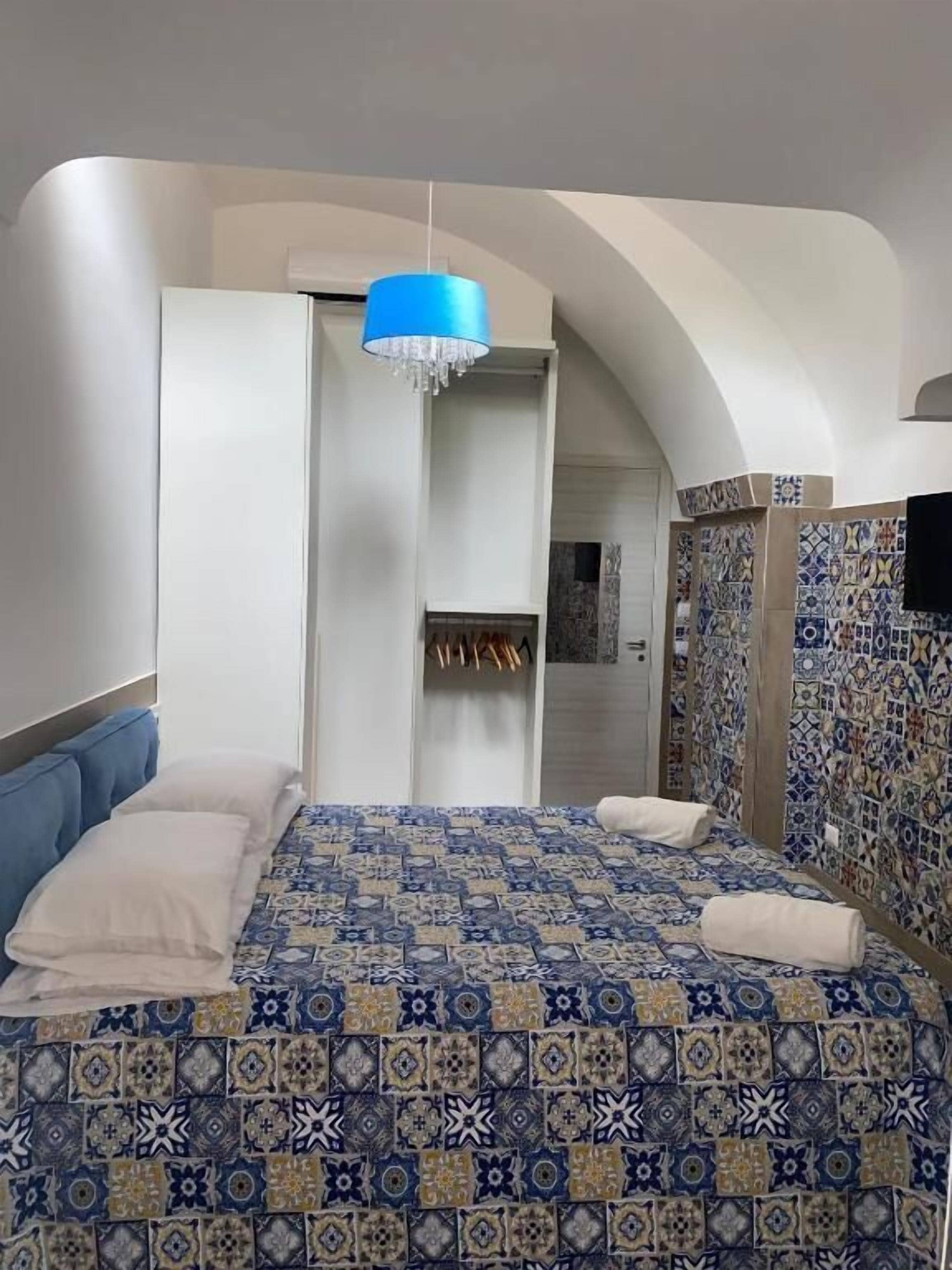 A bedroom with a patterned bedspread, a blue chandelier, and a wardrobe with a tiled wall.