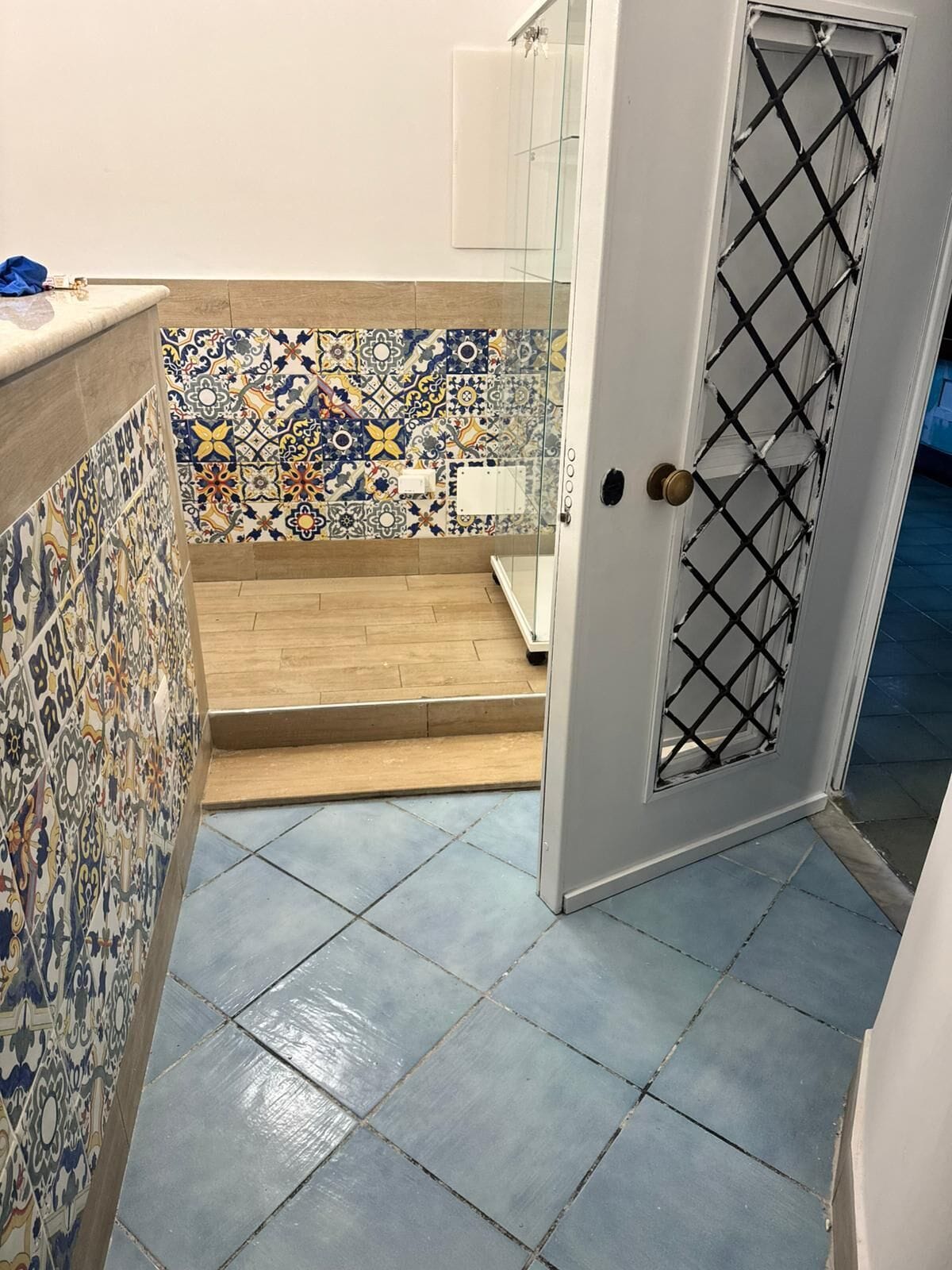 Un baño con piso de baldosas, zona de ducha y una puerta con mosquitero.