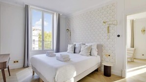 A modern bedroom with a large bed, a bedside table, and a window with curtains. - A Charming 2-BR/2BA - Montorgueil (Paris)