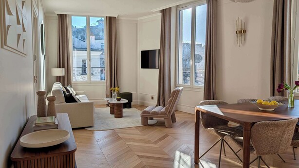 A modern living room with a sofa, armchair, dining table, and a TV mounted on the wall. - A Charming 2-BR/2BA - Montorgueil (Paris)