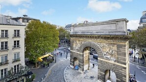 A historic stone archway with intricate carvings, surrounded by urban buildings and a cobblestone street. - A Charming 2-BR/2BA - Montorgueil (Paris)
