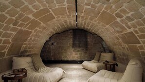 A stone-walled room with two cushioned seating areas and a small table. - An Exceptional 3-BR/3Ba with Services - Le Marais (Paris)