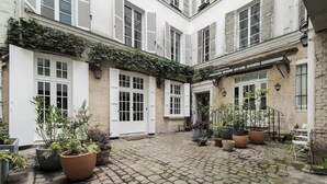 A courtyard with cobblestone flooring, potted plants, and white shutters on the buildings. - An Exceptional 3-BR/3Ba with Services - Le Marais (Paris)